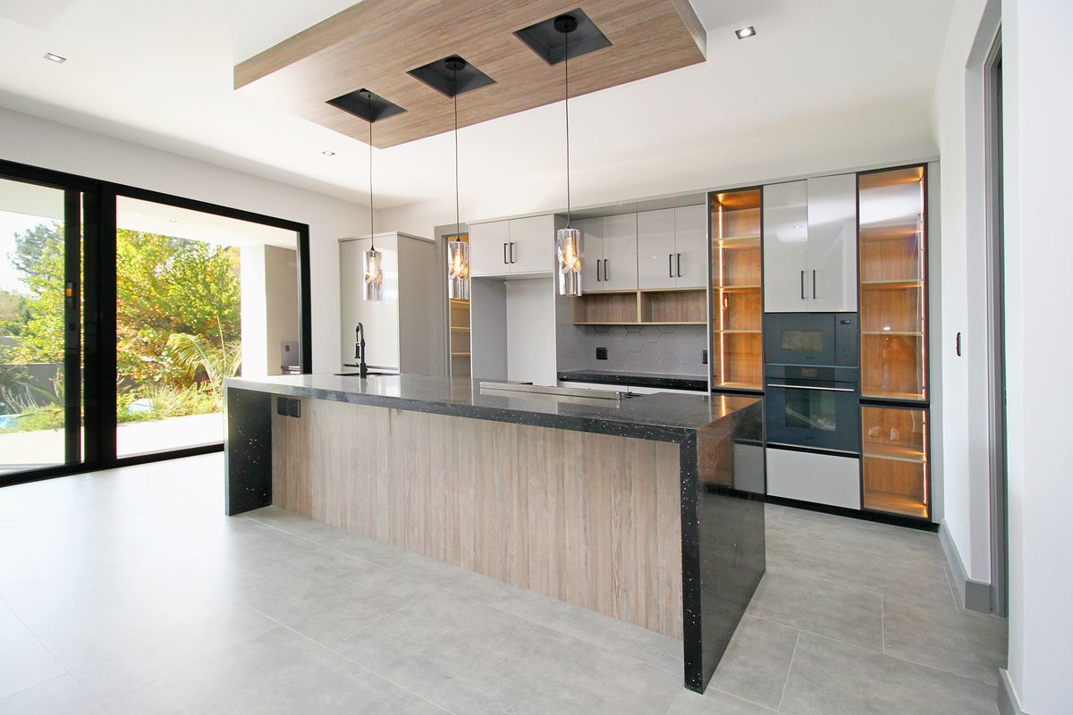Modern kitchen featuring a large island with stone countertops, integrated cabinetry, built-in oven, and seamless access to the outdoor patio through sliding glass doors.