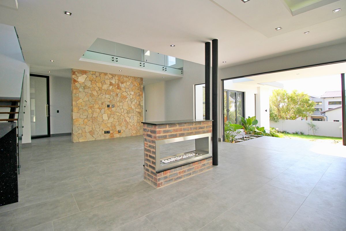 Spacious open-plan living area featuring a modern double-sided fireplace, stone feature wall, and seamless indoor-outdoor flow through large sliding glass doors.