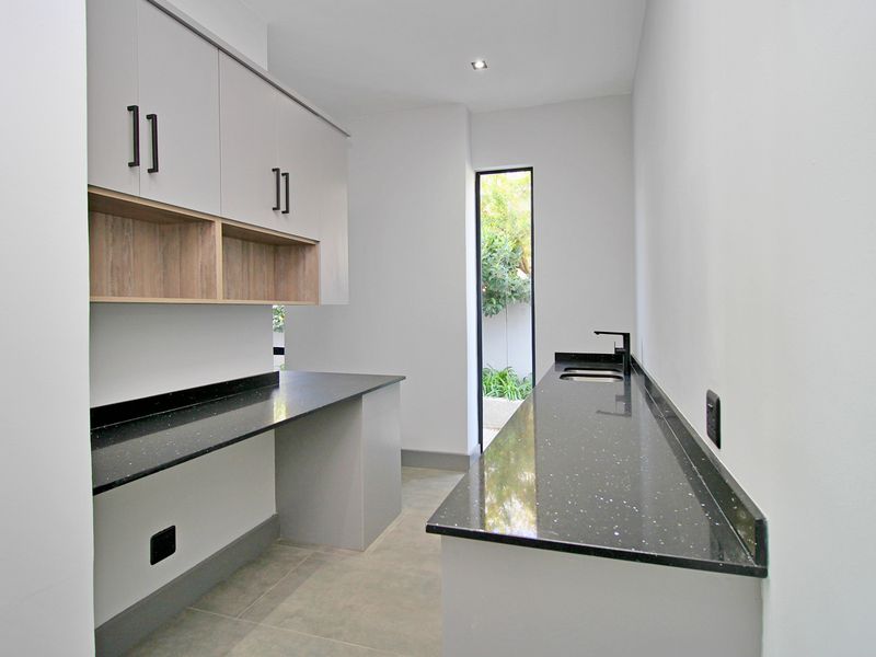 A modern, clean scullery featuring sleek cabinetry, dark stone countertops, an undermount sink, and direct access to an outdoor area.