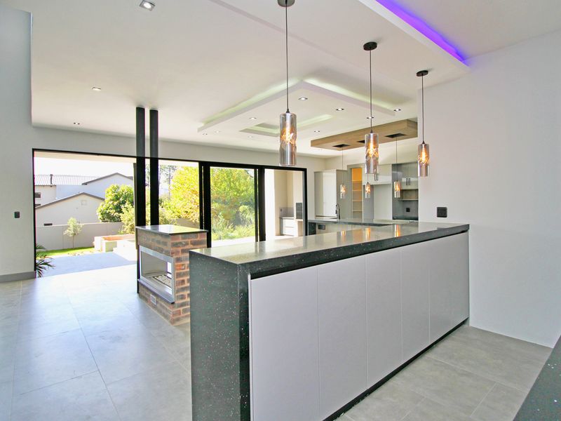 Modern open-plan living and kitchen area featuring a sleek island, built-in fireplace, recessed lighting, and large sliding doors opening to the garden.