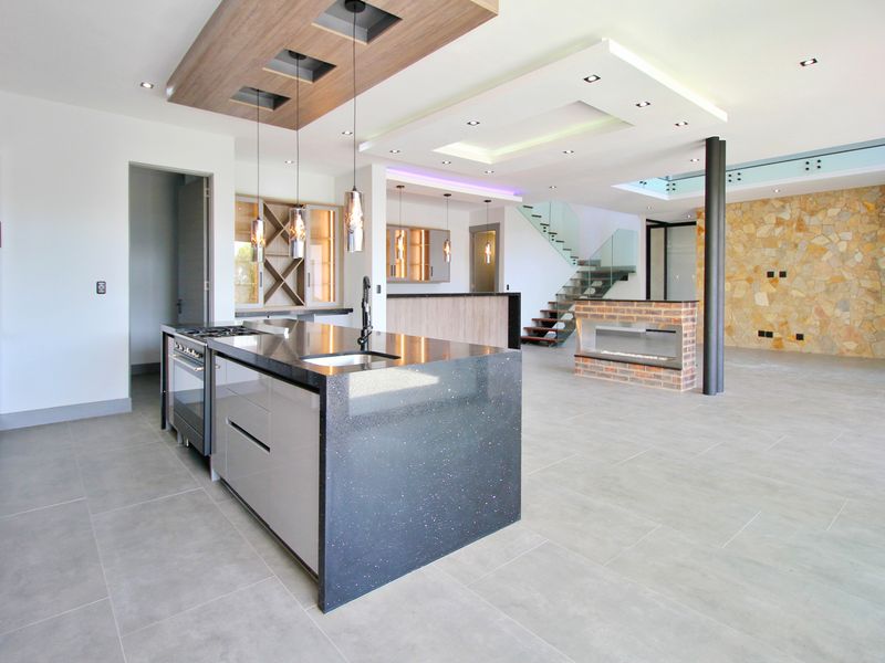 Spacious open-plan living area featuring a modern kitchen with stone island, built-in fireplace, stone feature wall, and a contemporary glass staircase.