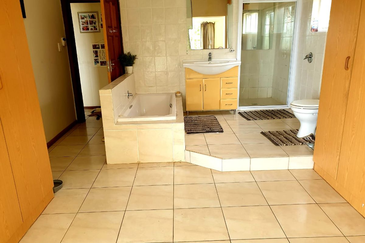 A spacious bathroom featuring a built-in bathtub, separate shower enclosure, vanity unit, and built-in storage cupboards with tiled finishes throughout.