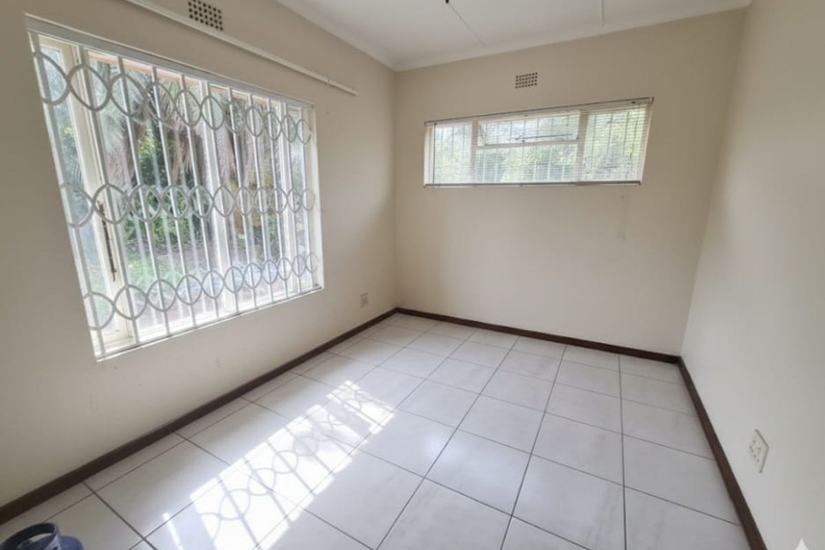 A bright, empty bedroom featuring neutral tiled flooring, a ceiling fan, and security bars on the windows.
