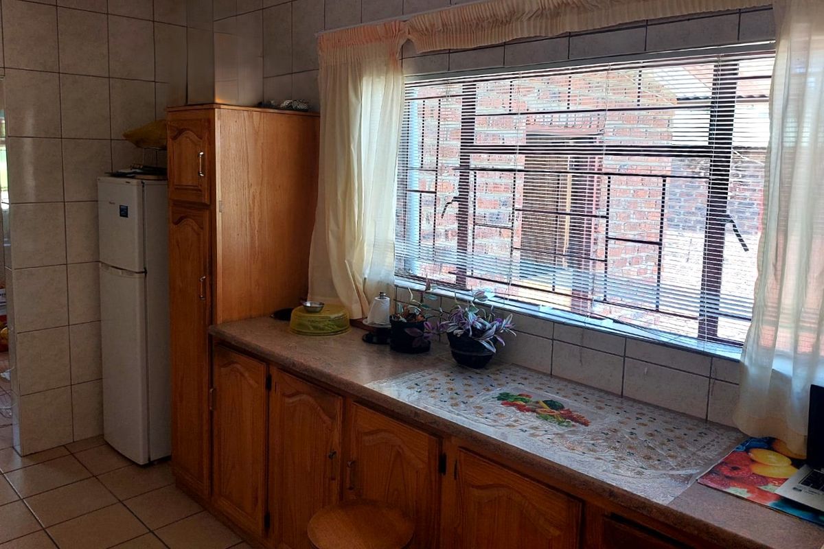 A functional kitchen featuring wooden cabinetry, tiled walls, and a window with security bars, providing a practical workspace with ample storage.