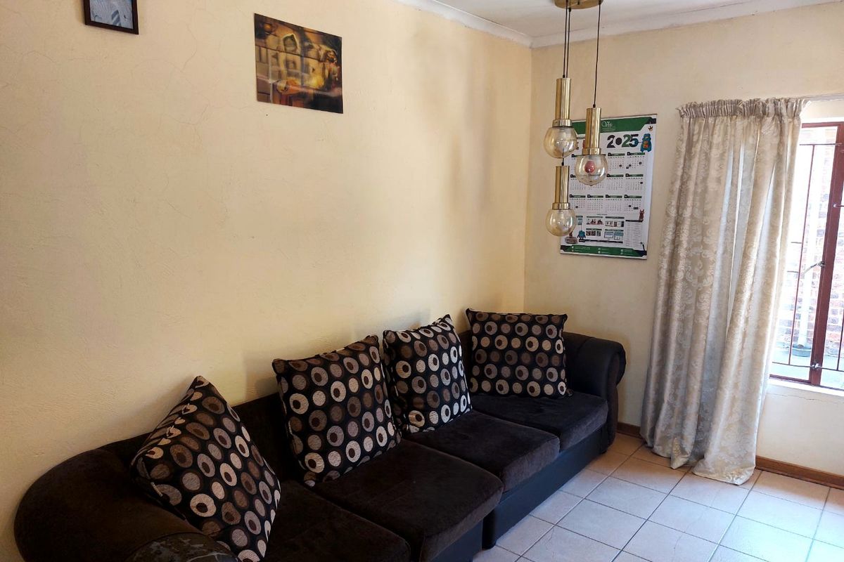 A living room area featuring tiled flooring, a decorative pendant light fixture, and a window with curtain treatments.