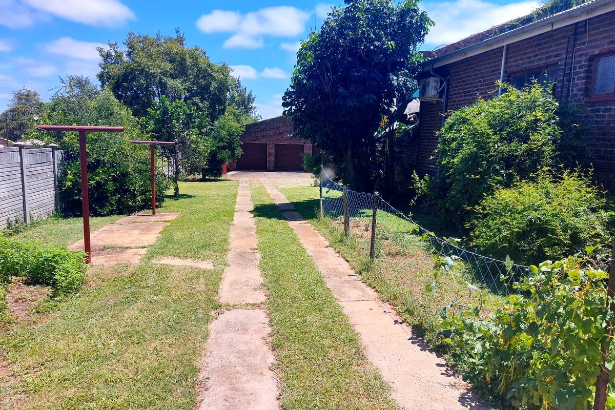 A spacious rear garden featuring a concrete driveway leading to a detached double garage, with established trees and lawn area.