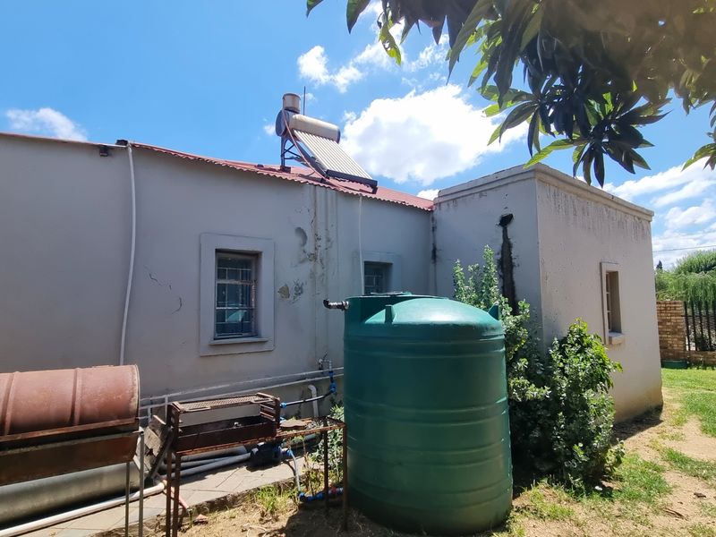 Rear exterior view of the property featuring a solar water heater, water storage tank, and visible wear to the exterior wall finishes.
