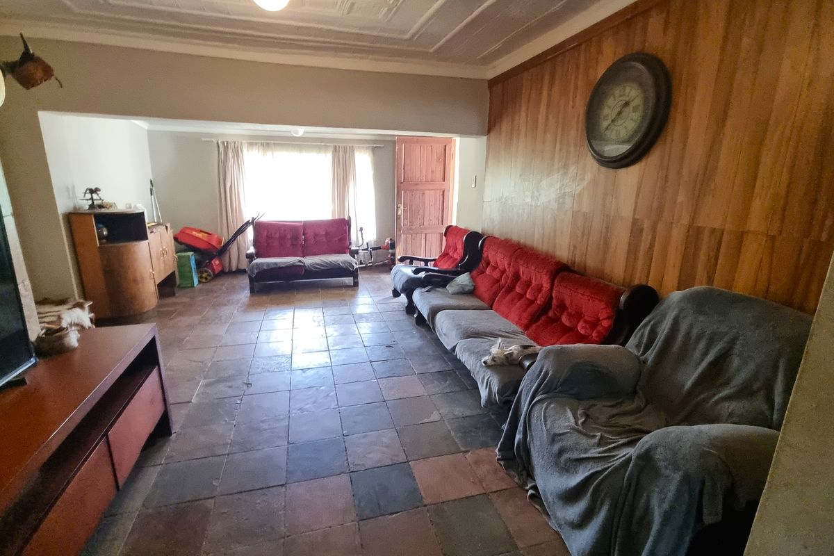 Spacious living area featuring traditional wood paneling, decorative ceiling details, and durable tiled flooring, offering a dated but functional layout.