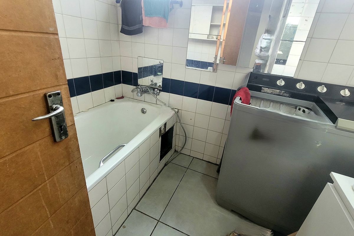 A functional bathroom featuring a built-in bathtub with tiled surround and wall-mounted mirror, requiring some maintenance and cosmetic updates.
