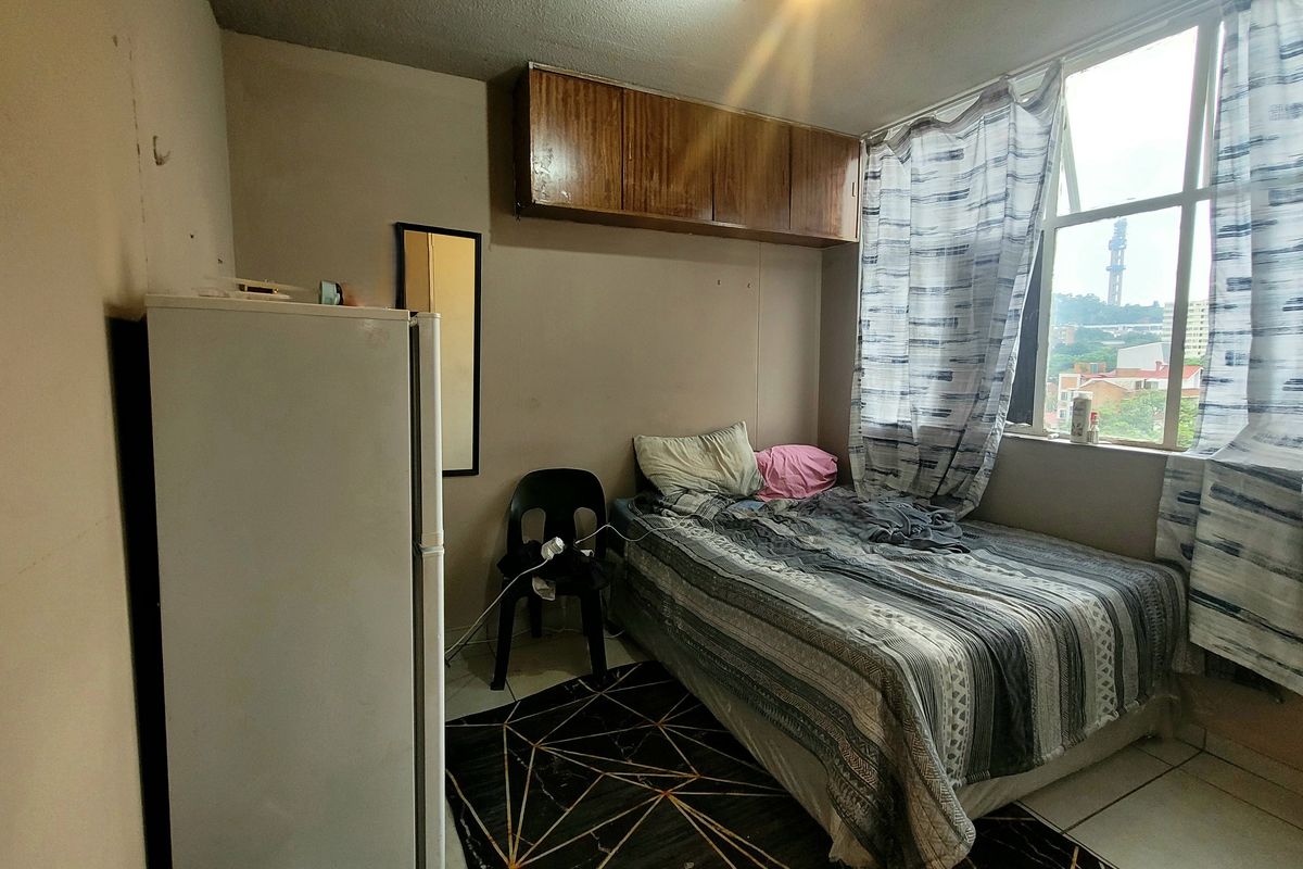 A compact bedroom featuring built-in overhead storage cabinetry and a large window providing natural light and urban views.