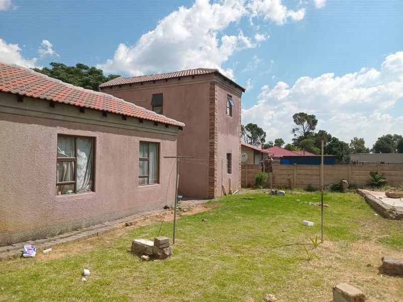 Rear view of the property featuring a multi-level structure with tiled roofing, plastered walls, and a spacious backyard with boundary walling.
