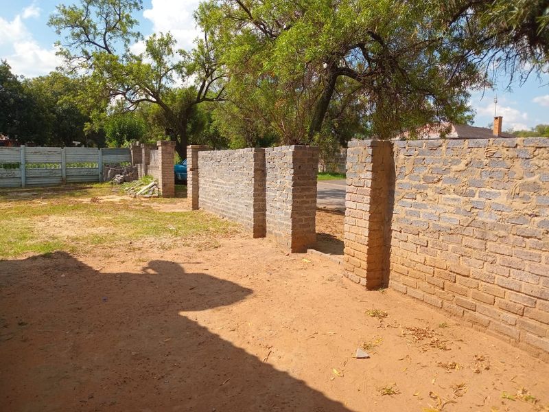 An exterior view showing an unfinished brick boundary wall and precast concrete fencing on a property with unlandscaped ground.