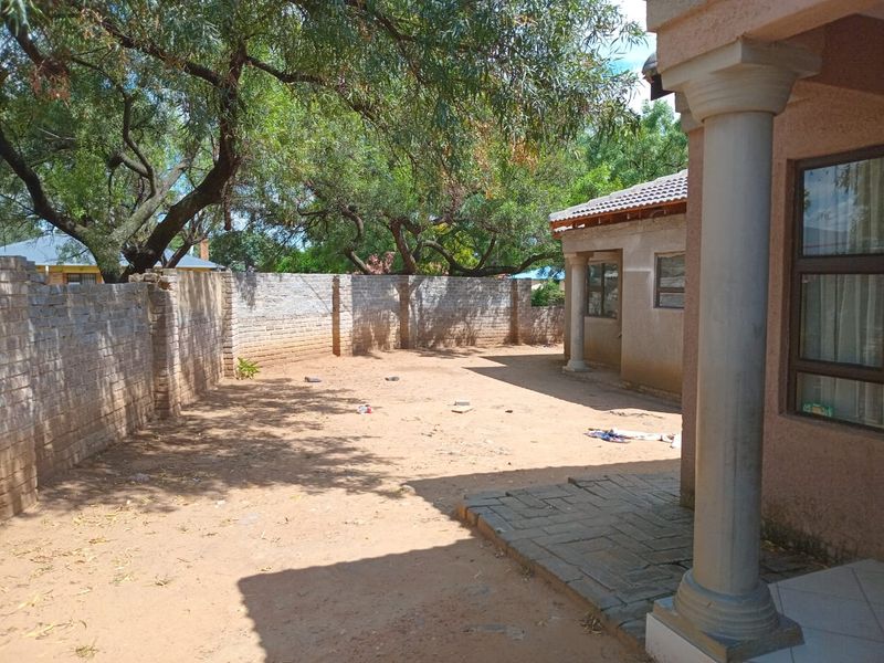 Rear exterior view of the property featuring a paved patio, concrete columns, and a large, unlandscaped garden area enclosed by a brick boundary wall.