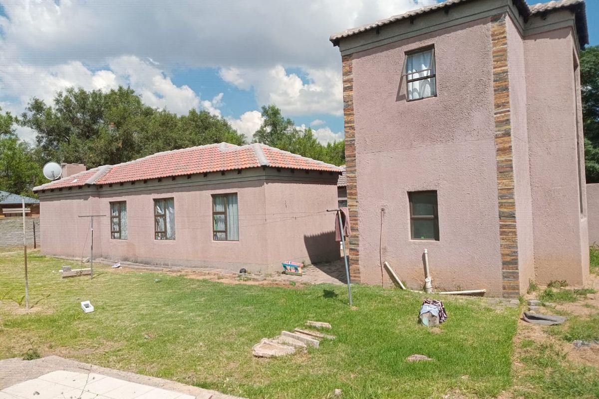 Rear view of the property featuring a multi-level structure with plastered walls, stone cladding accents, and a tiled roof set against a garden area.