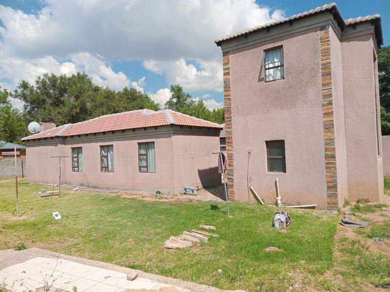 Rear view of the property featuring a multi-level structure with plastered walls, stone cladding accents, and a tiled roof set against a garden area.