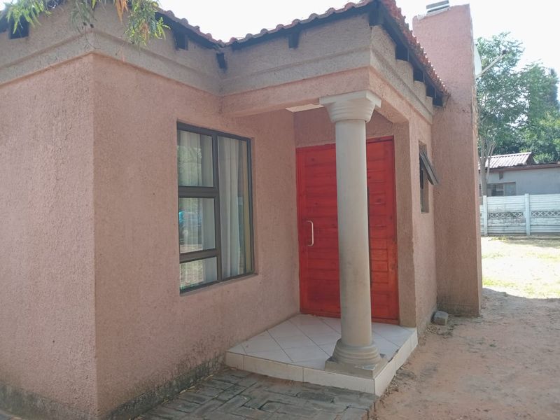 Front entrance of a house featuring a tiled porch, a decorative column, and a bright red timber door with aluminium window frames.
