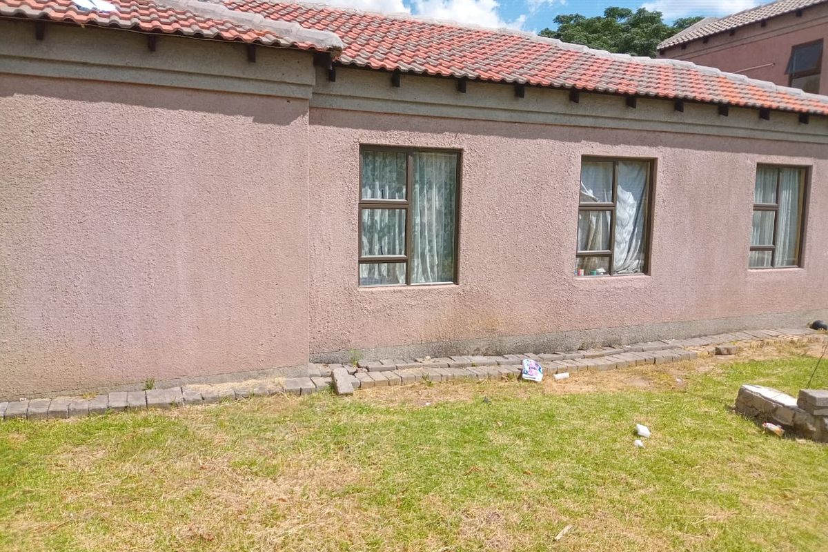 Rear exterior view of the house featuring a terracotta tiled roof, stucco walls, and aluminium window frames overlooking a garden area.