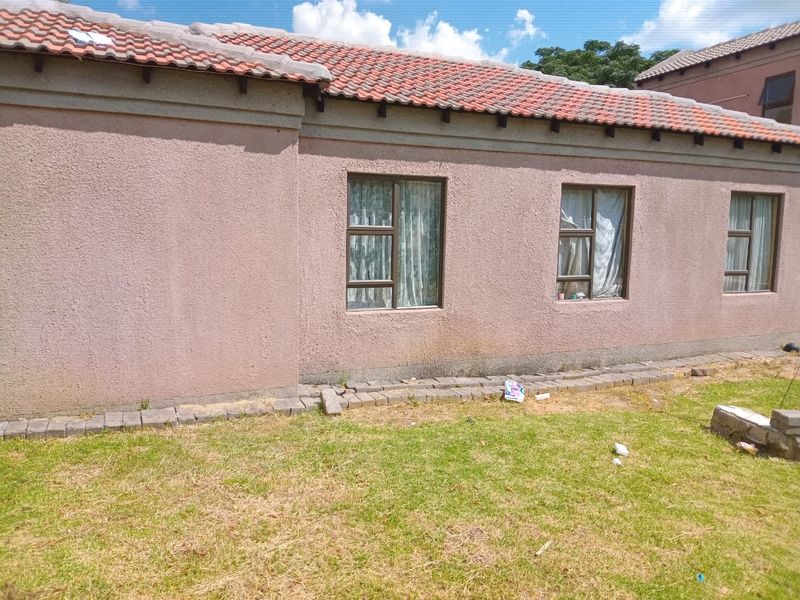 Rear exterior view of the house featuring a terracotta tiled roof, stucco walls, and aluminium window frames overlooking a garden area.