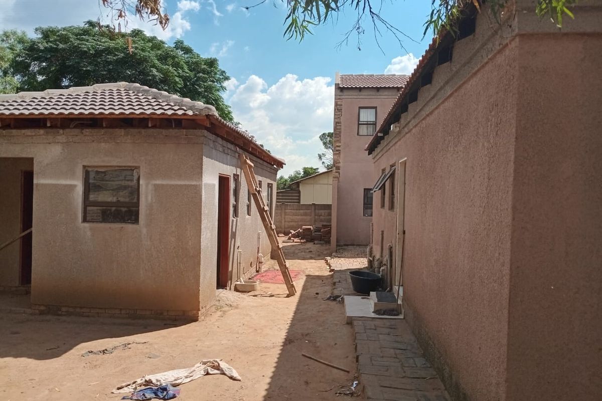 Rear view of the property showing multiple structures with unfinished exterior plastering and exposed roof rafters in a yard setting.