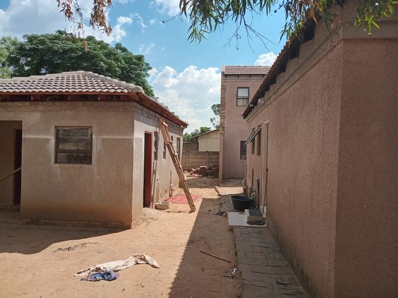Rear view of the property showing multiple structures with unfinished exterior plastering and exposed roof rafters in a yard setting.