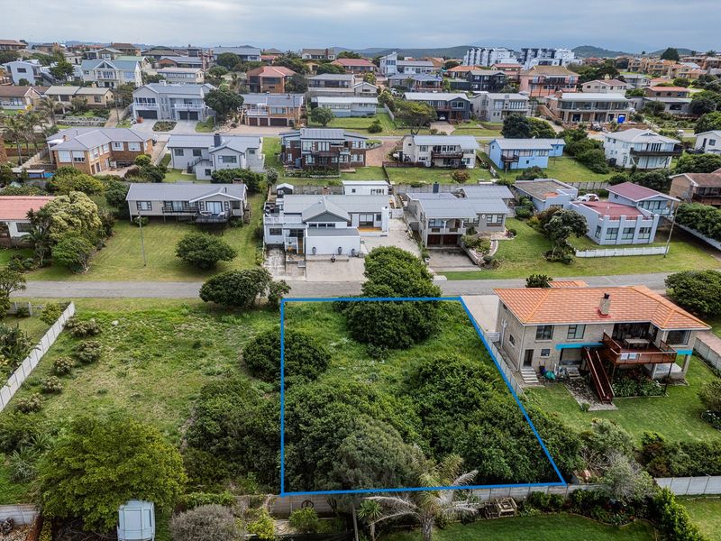 An aerial view of a vacant residential plot situated in a developed coastal neighborhood, featuring established vegetation and clear boundary lines.