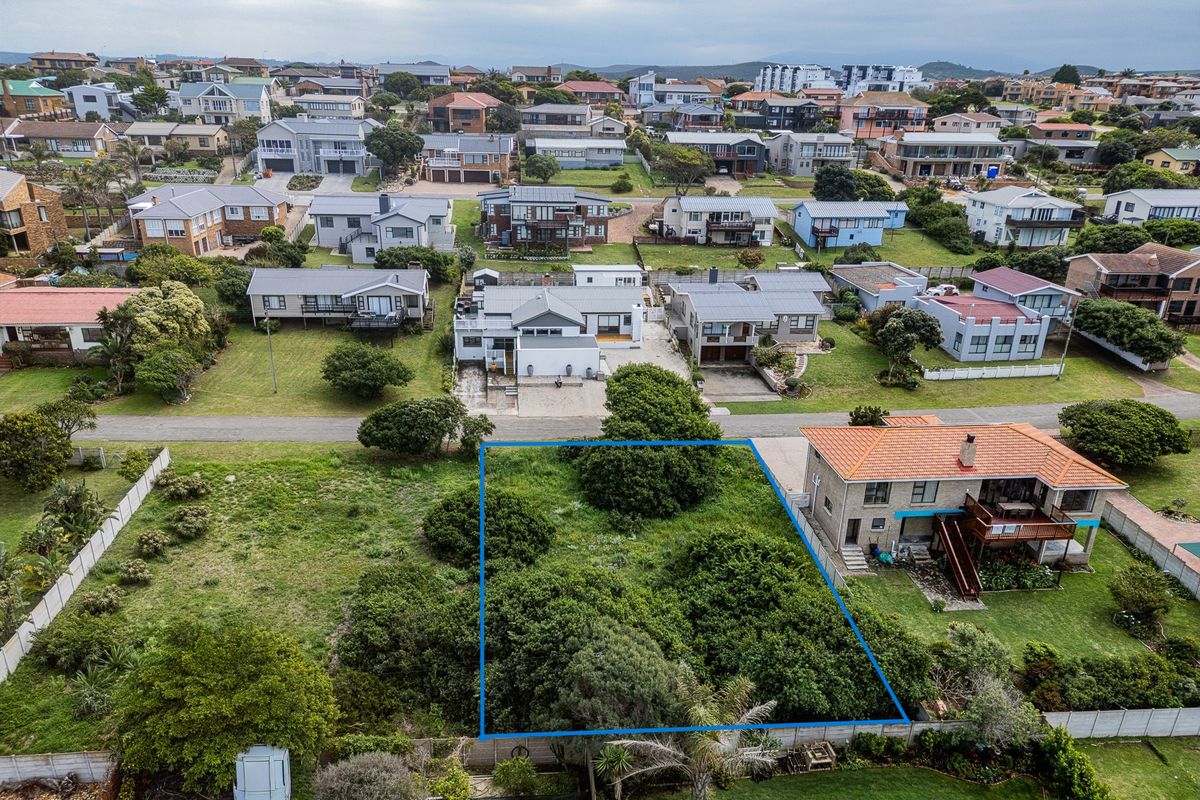 An aerial view of a vacant residential plot situated in a developed coastal neighborhood, featuring established vegetation and clear boundary lines.