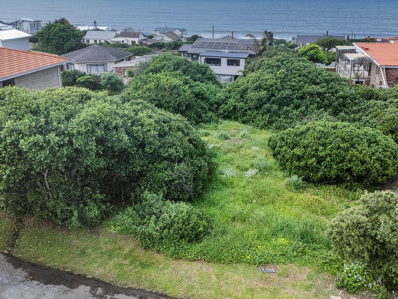 An elevated aerial view of a vacant residential plot featuring established coastal vegetation, situated in a developed neighborhood near the ocean.