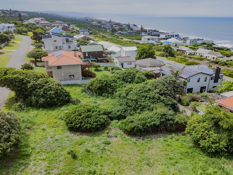 An aerial view of a vacant residential plot situated in a coastal neighborhood, surrounded by established homes and natural vegetation.