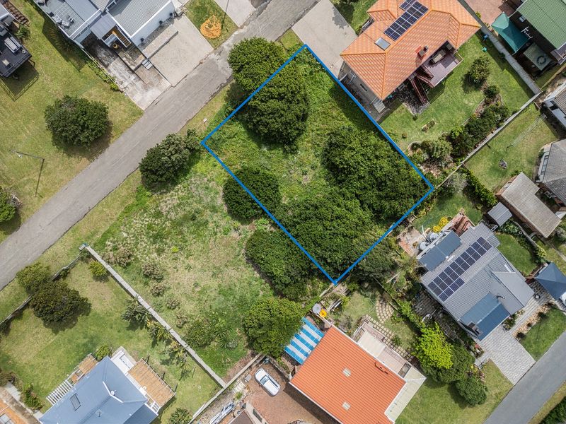 An aerial view of a vacant residential plot featuring established trees, situated within an established neighborhood.