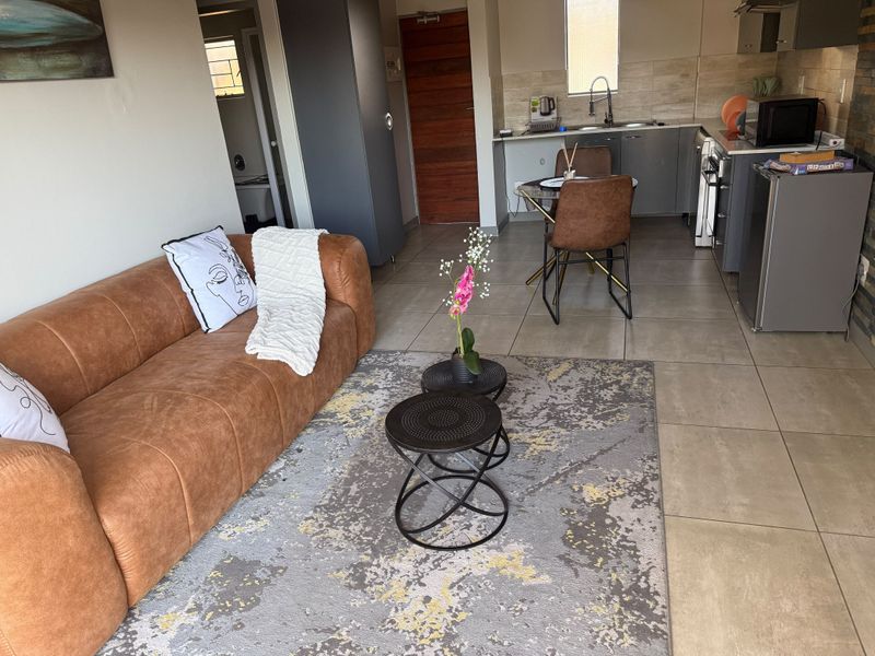 An open-plan living and kitchen area featuring neutral tiled flooring, modern grey kitchen cabinetry, and a functional layout suitable for compact apartment living.