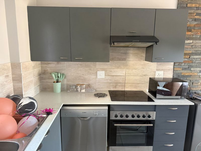 Modern kitchen featuring grey cabinetry, stone-look tile backsplash, integrated extractor fan, electric hob, built-in oven, and a stylish stacked stone feature wall.