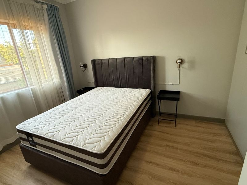 A well-maintained bedroom featuring laminate flooring and wall-mounted lighting, offering a clean and functional space.