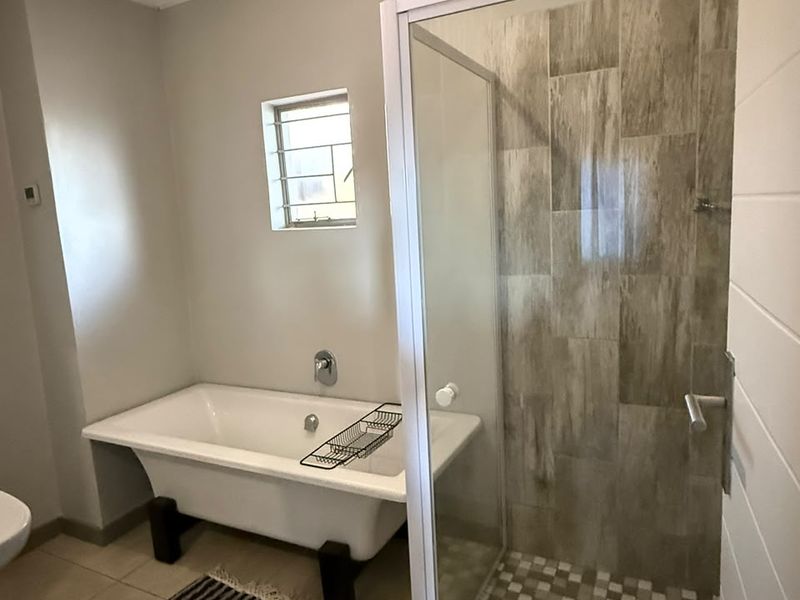 A well-maintained bathroom featuring a classic freestanding bathtub, a separate walk-in shower with tiled walls, and neutral floor tiling.