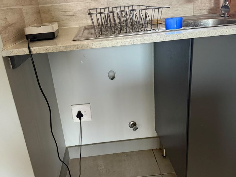 A laundry area featuring a stainless steel sink, stone countertop, and tiled backsplash, currently showing exposed plumbing and missing cabinetry.