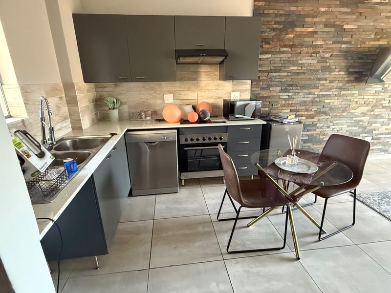 Modern kitchen featuring dark grey cabinetry, stone countertops, integrated appliances, and a decorative stone-clad feature wall, creating a contemporary and functional cooking space.