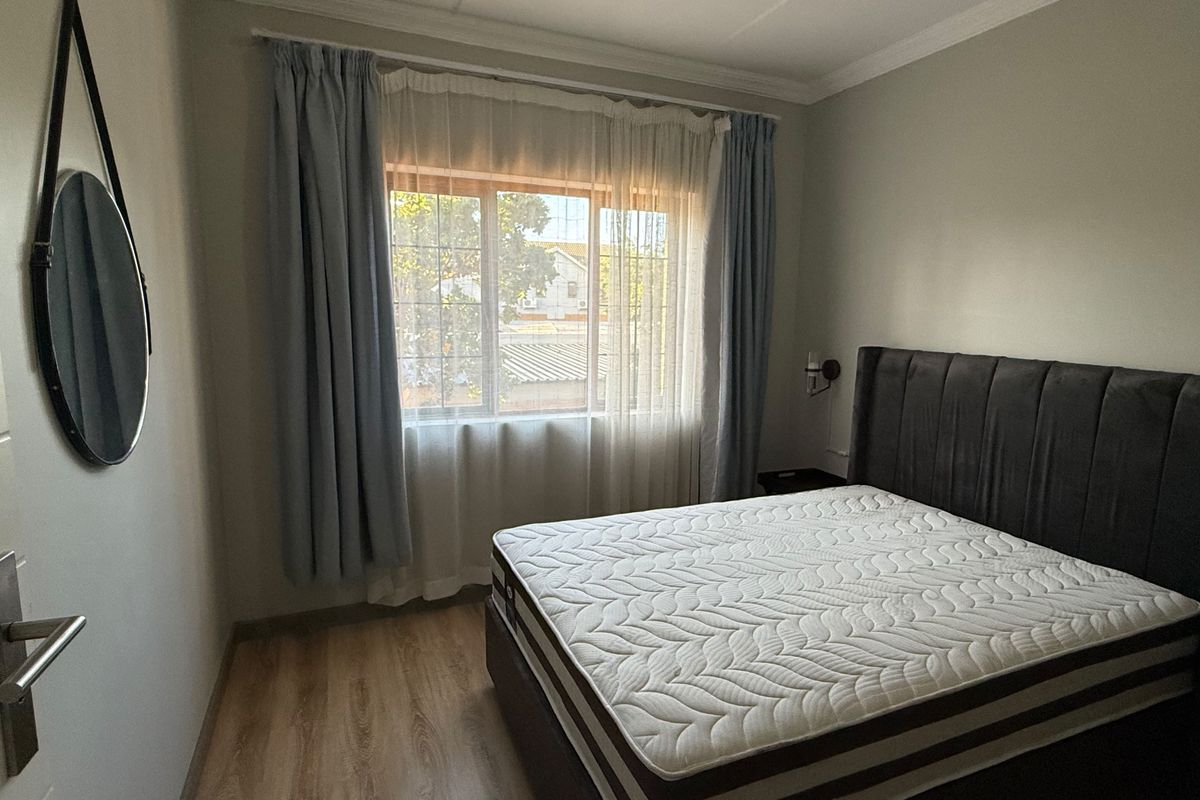 A well-lit bedroom featuring laminate flooring, neutral wall finishes, and a classic cove cornice detail.