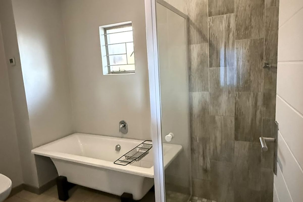 A well-maintained bathroom featuring a classic freestanding bathtub, a separate walk-in shower with tiled walls, and neutral floor tiling.