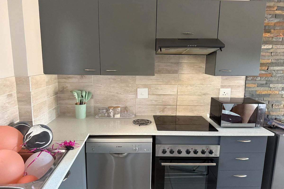 Modern kitchen featuring grey cabinetry, stone-look tile backsplash, integrated extractor fan, electric hob, built-in oven, and a stylish stacked stone feature wall.