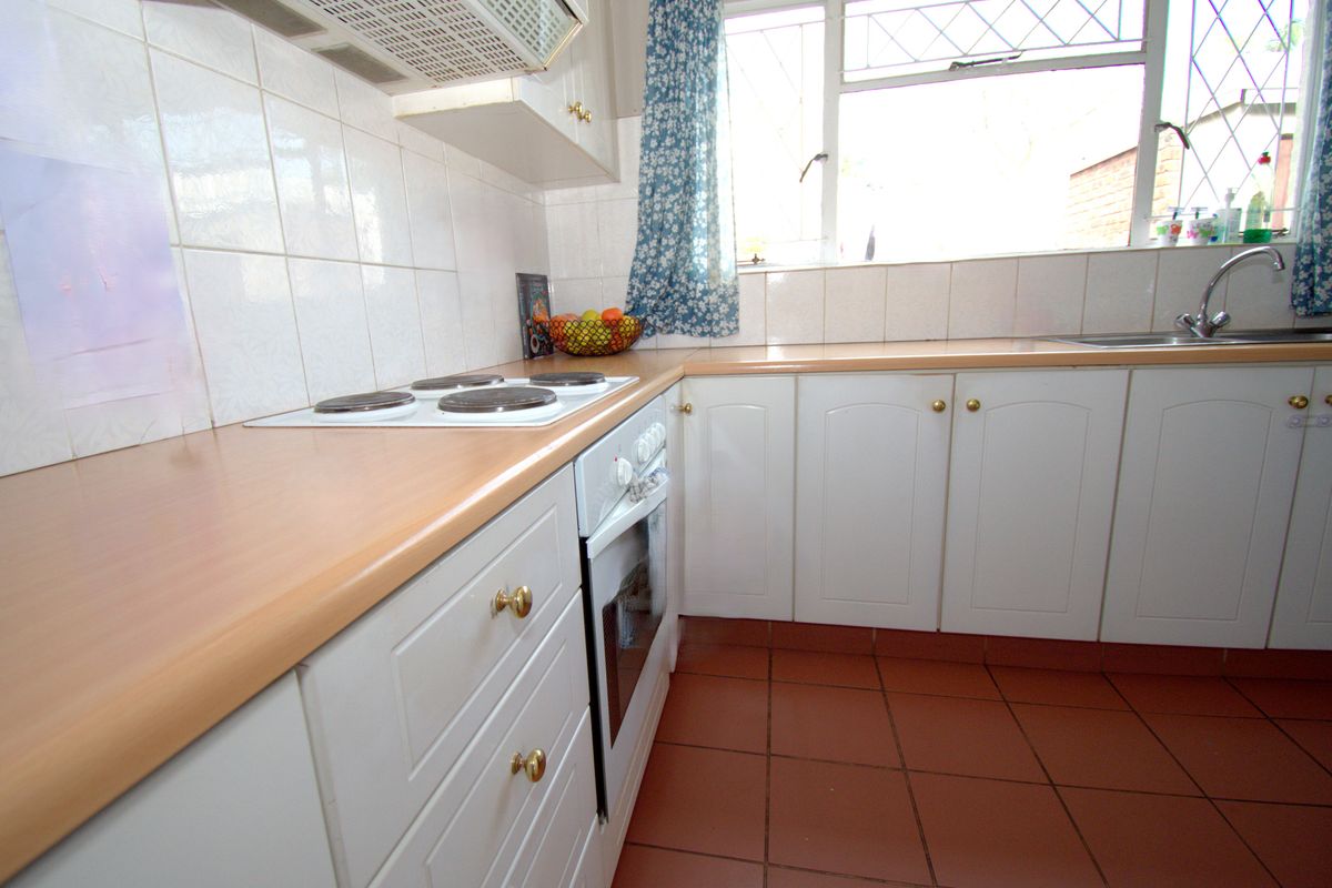 A functional kitchen featuring white cabinetry, laminate countertops, an electric hob, built-in oven, and tiled flooring with a window overlooking the exterior.