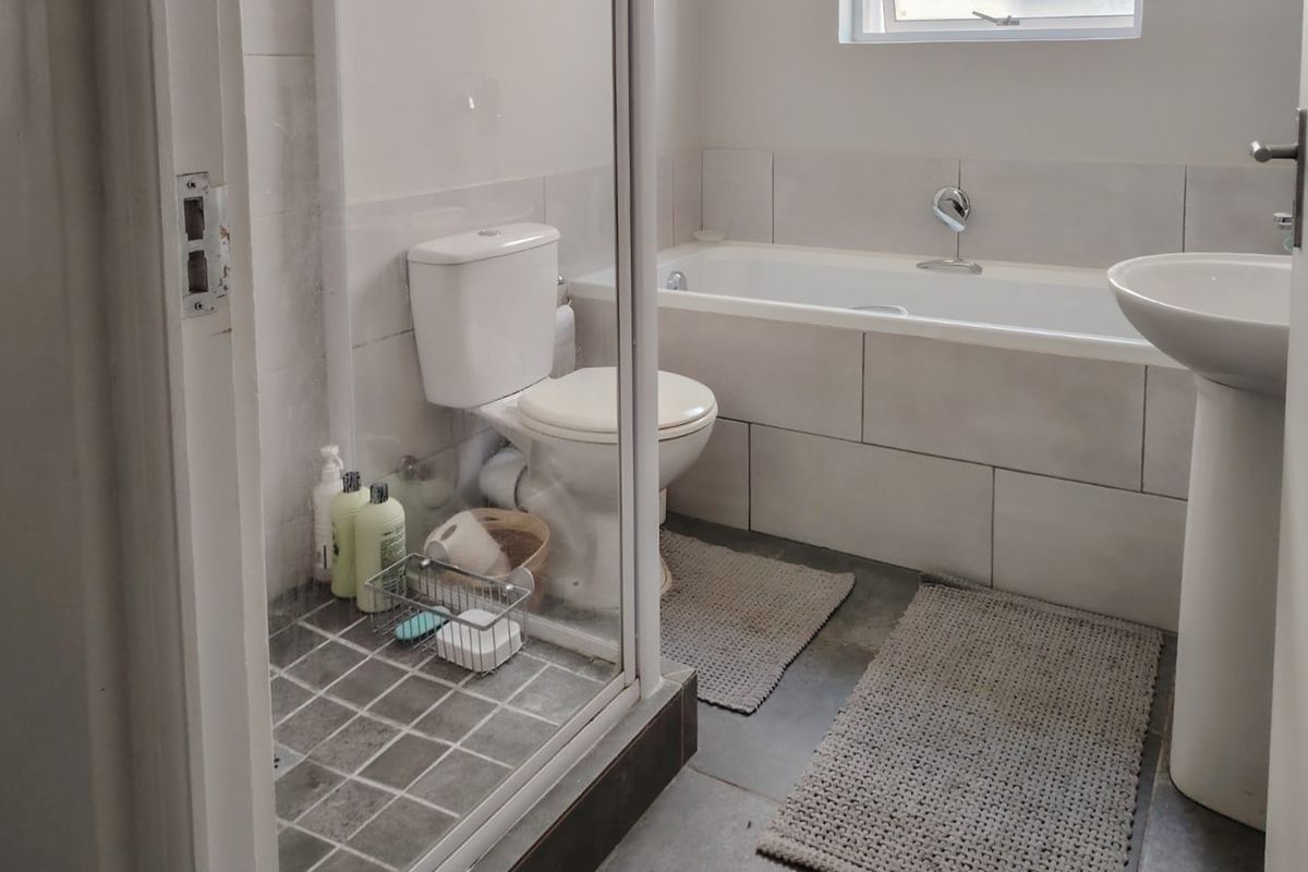 A functional bathroom featuring a shower enclosure, bathtub, and pedestal basin with neutral wall and floor tiling.