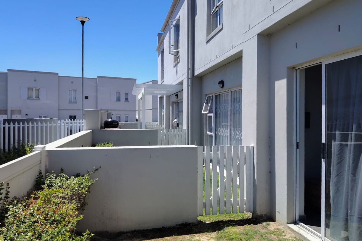 Rear view of the townhouse featuring a private patio area with low masonry walls, a white picket gate, and sliding door access to the interior.