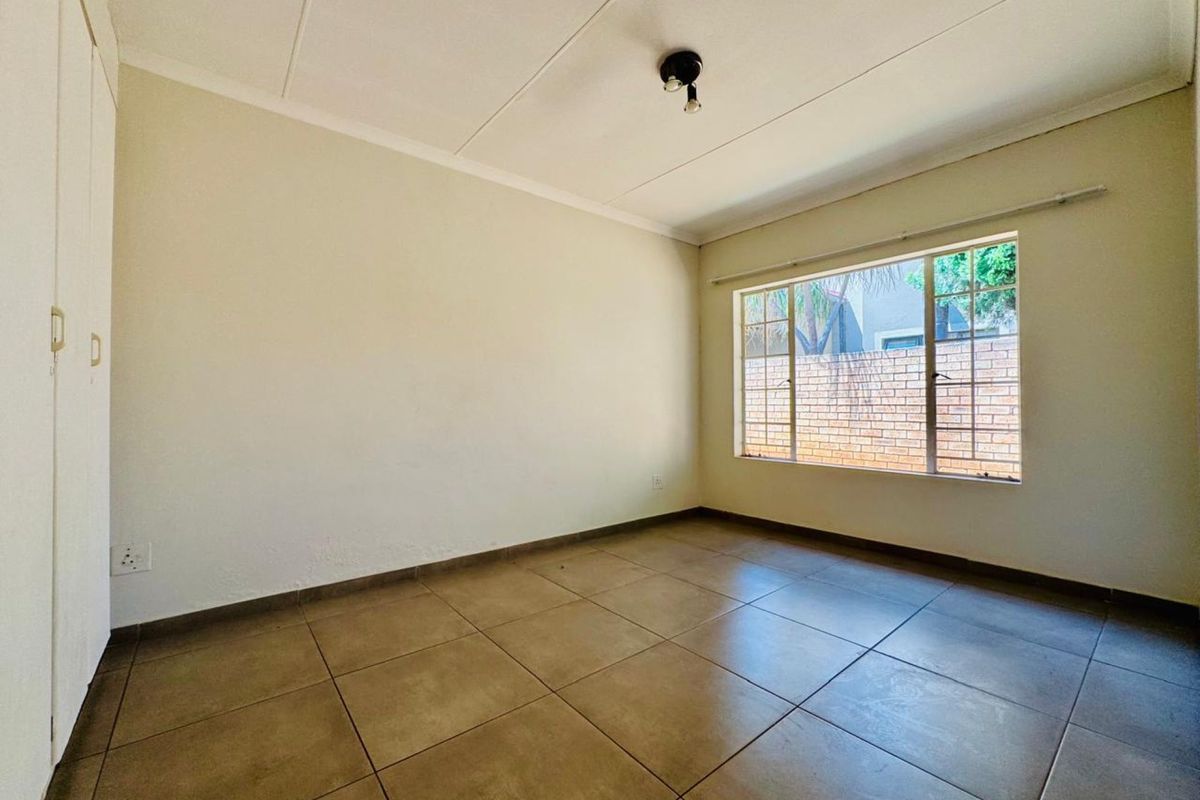 A bright, empty bedroom featuring neutral tiled flooring, built-in cupboards, and a large window providing natural light.