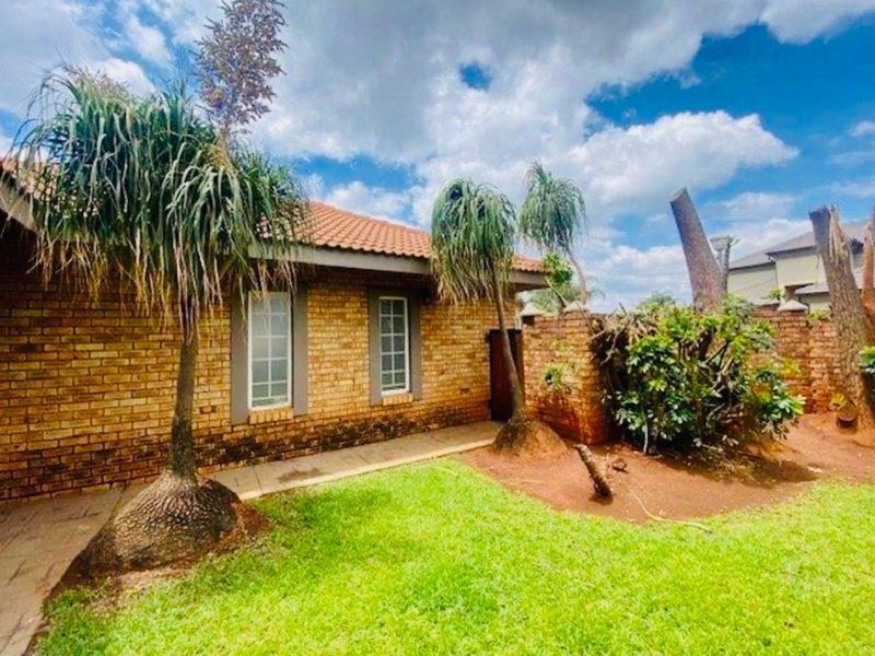Rear exterior view of a face brick house featuring a tiled roof, paved walkway, and established garden area with boundary wall.