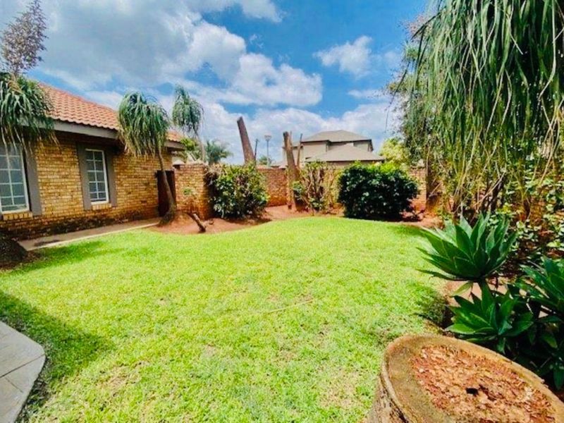 A private rear garden featuring a well-maintained lawn, brick boundary walls, and a view of the home's exterior brick facade.