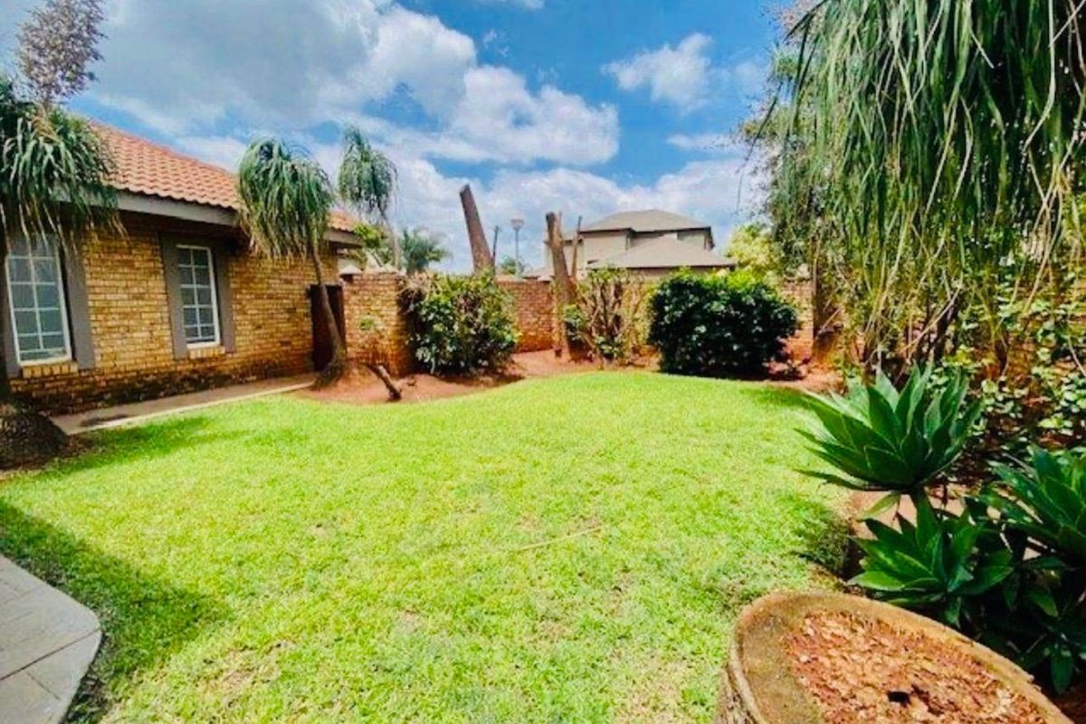A private rear garden featuring a well-maintained lawn, brick boundary walls, and a view of the home's exterior brick facade.