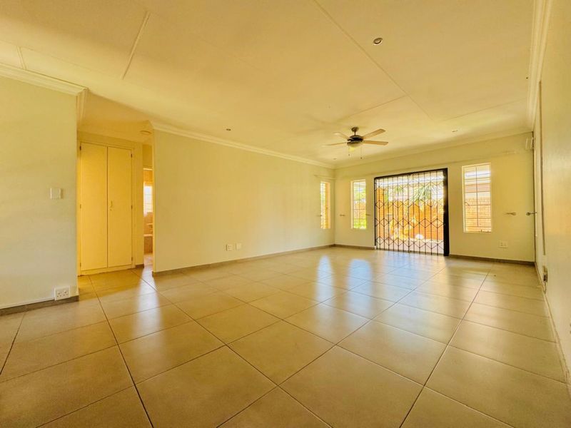 Spacious, light-filled living area featuring neutral tiled flooring, a ceiling fan, and direct access to the outdoor area through a secure sliding door.