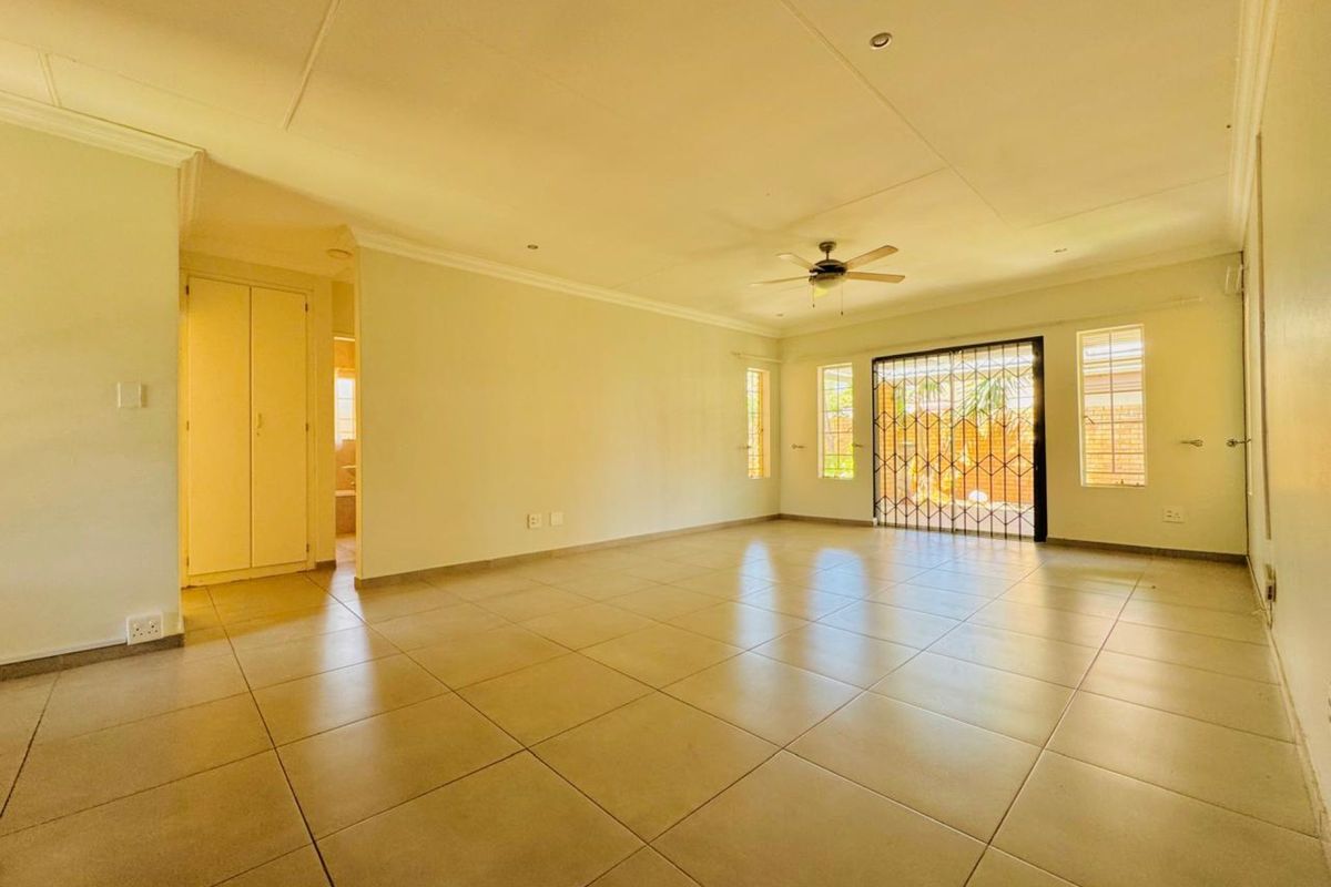 Spacious, light-filled living area featuring neutral tiled flooring, a ceiling fan, and direct access to the outdoor area through a secure sliding door.