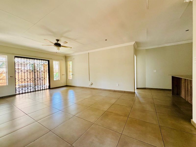 Spacious open-plan living area featuring neutral tiled flooring, a ceiling fan, and a breakfast bar, offering a versatile layout for modern living.