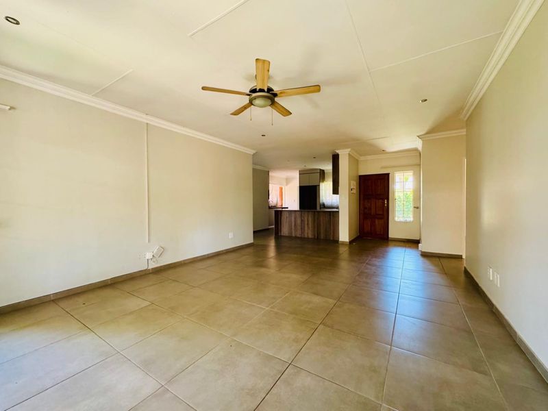 Spacious open-plan living area featuring neutral tiled flooring, a ceiling fan, and a functional kitchen layout with a central island.