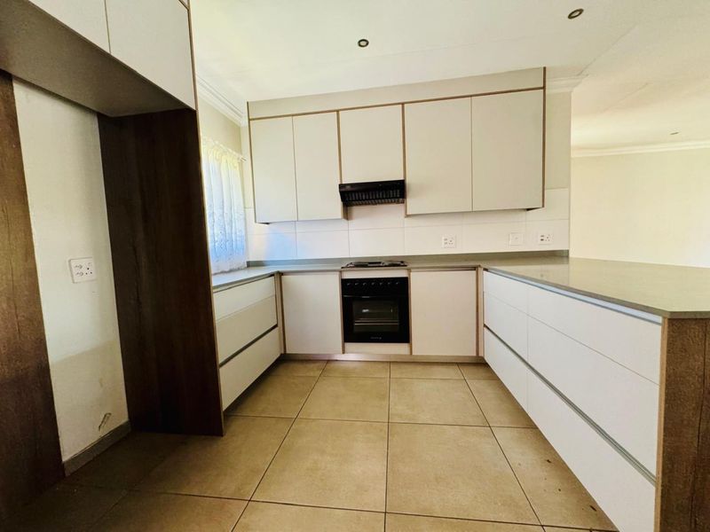 Modern kitchen featuring clean white cabinetry, stone countertops, tiled flooring, and integrated appliances including an oven, hob, and extractor fan.